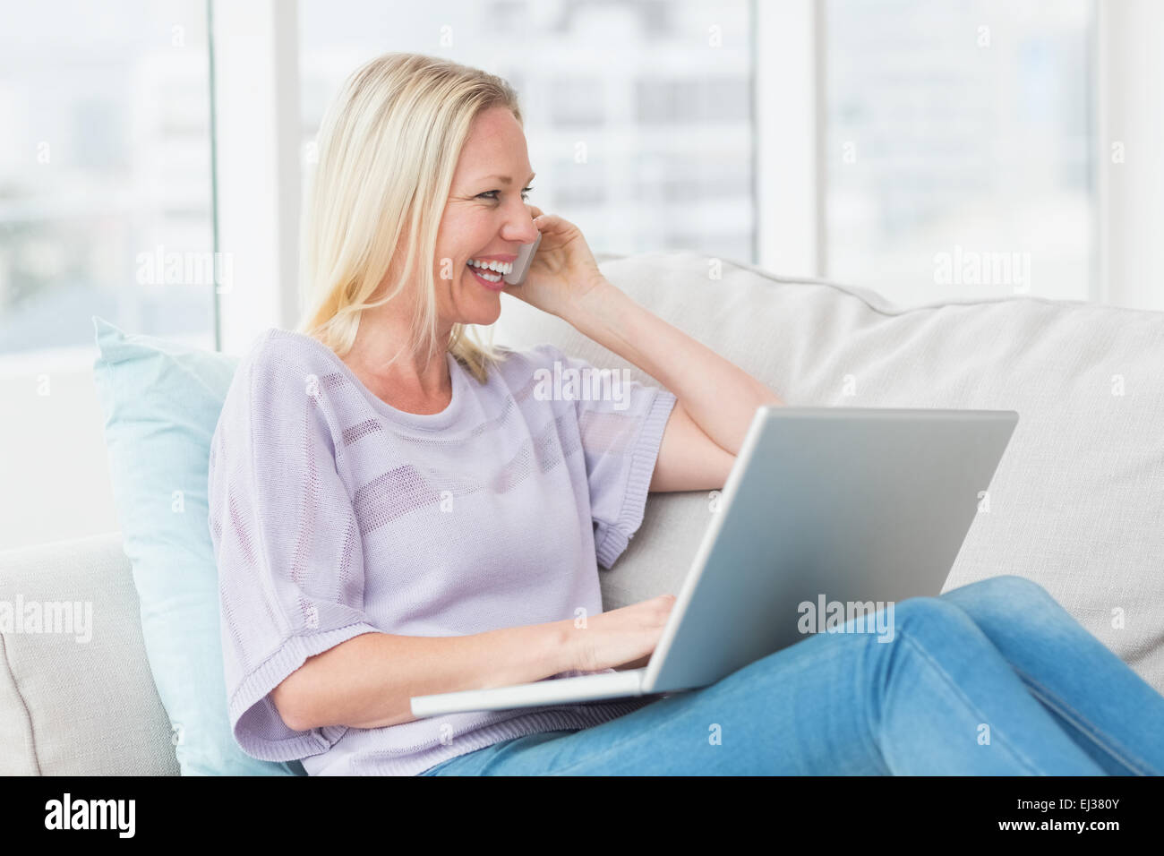 Frau am Handy während mit Laptop auf sofa Stockfoto