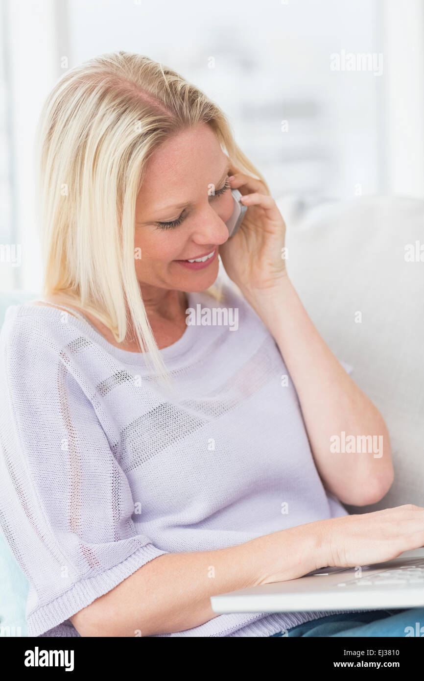 Frau am Handy während mit Laptop zu Hause Stockfoto