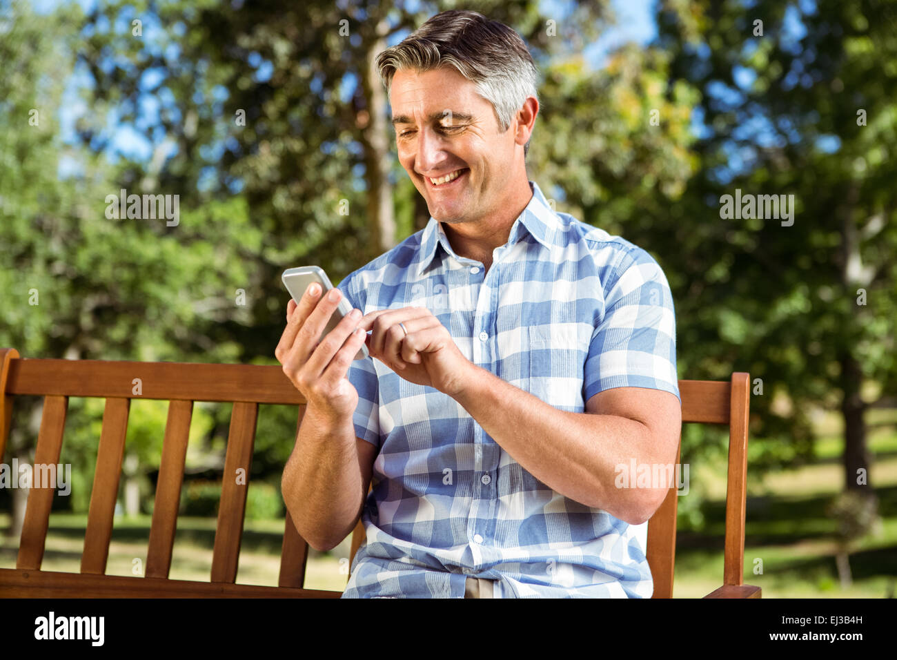 Mann sitzt auf der Parkbank mit Telefon Stockfoto