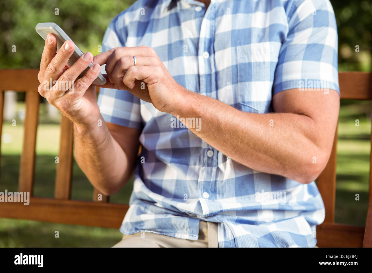 Mann sitzt auf der Parkbank mit Telefon Stockfoto