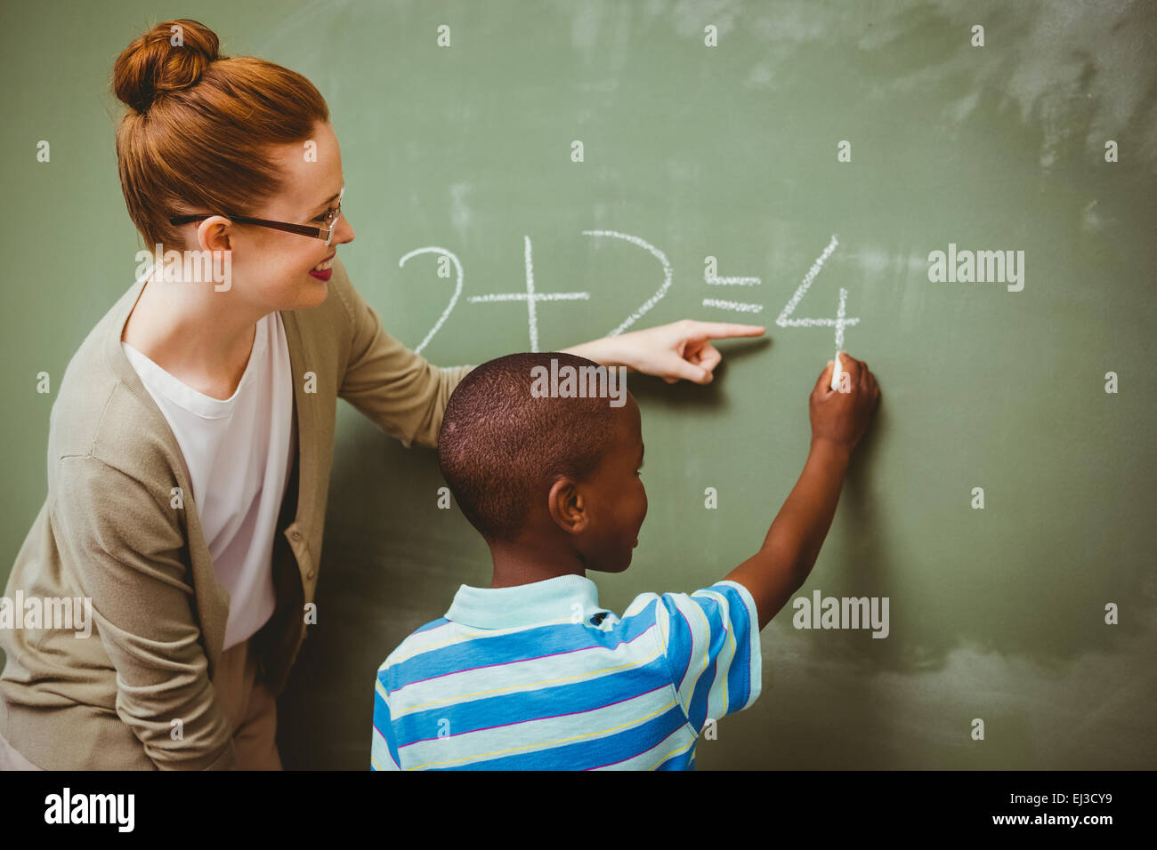 Lehrer, die Unterstützung der jungen zu schreiben auf der Tafel im Klassenzimmer Stockfoto