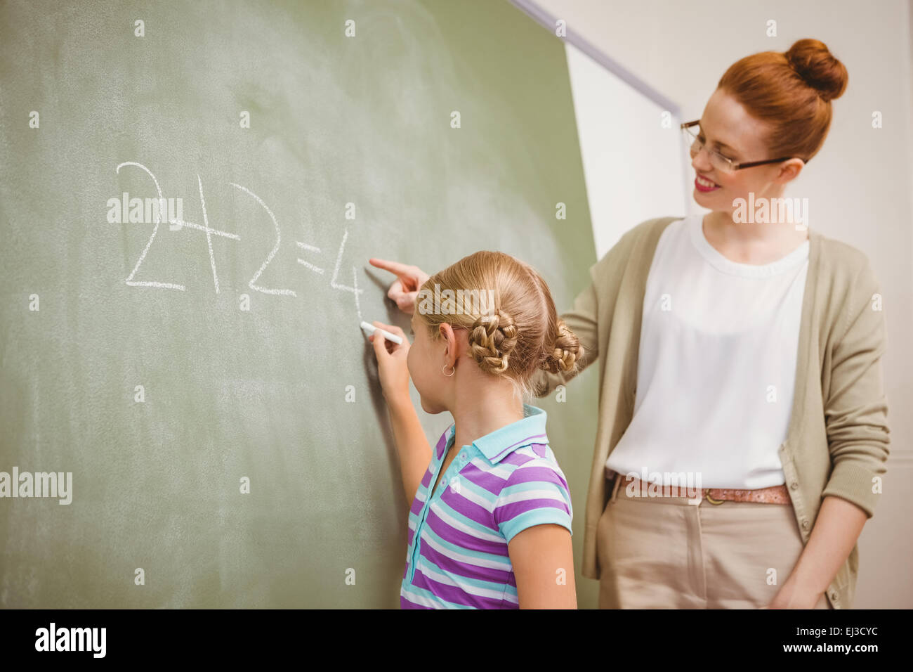 Lehrer, die Unterstützung von Mädchen zu schreiben auf der Tafel im Klassenzimmer Stockfoto