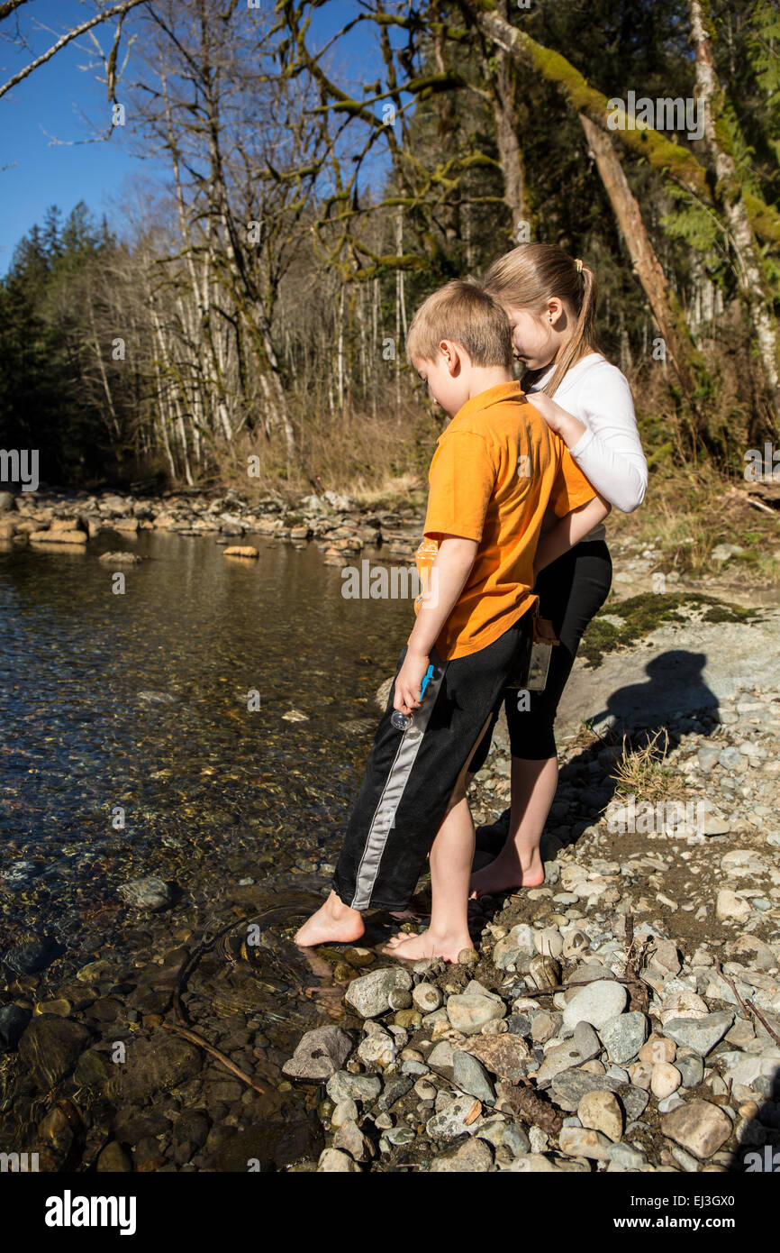 Sieben Jahre alter Junge und seine neunjährige Schwester behutsam die Kälte der Snoqualmie River, mit ihren Zehen testen Stockfoto