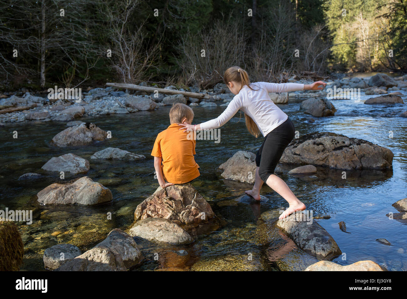 Neunjähriges Mädchen balancieren auf ihrem siebenjährigen Bruder Schulter, wie sie über Felsen in den seichten Fluss steigt Stockfoto