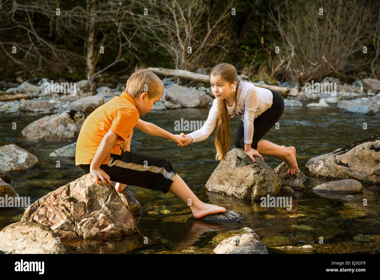 Neunjähriges Mädchen ermutigen ihr sieben Jahre alten Bruder, wie Sie vorwärts über die Felsen in der flachen Fluss zu kommen Stockfoto