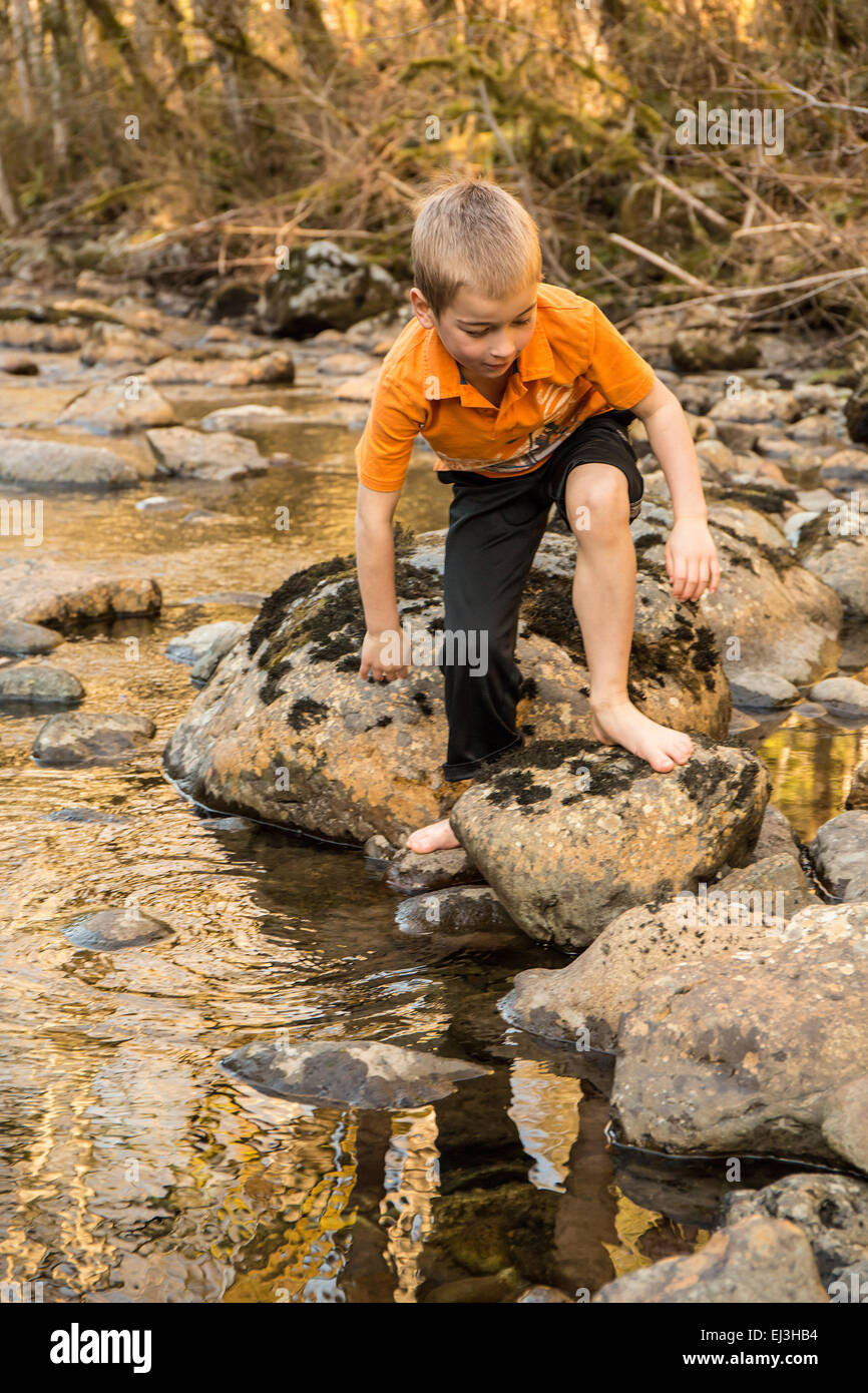 Sieben Jahre alten barfuß junge Klettern auf Felsen in Snoqualmie River in der Nähe von North Bend, Washington, USA Stockfoto