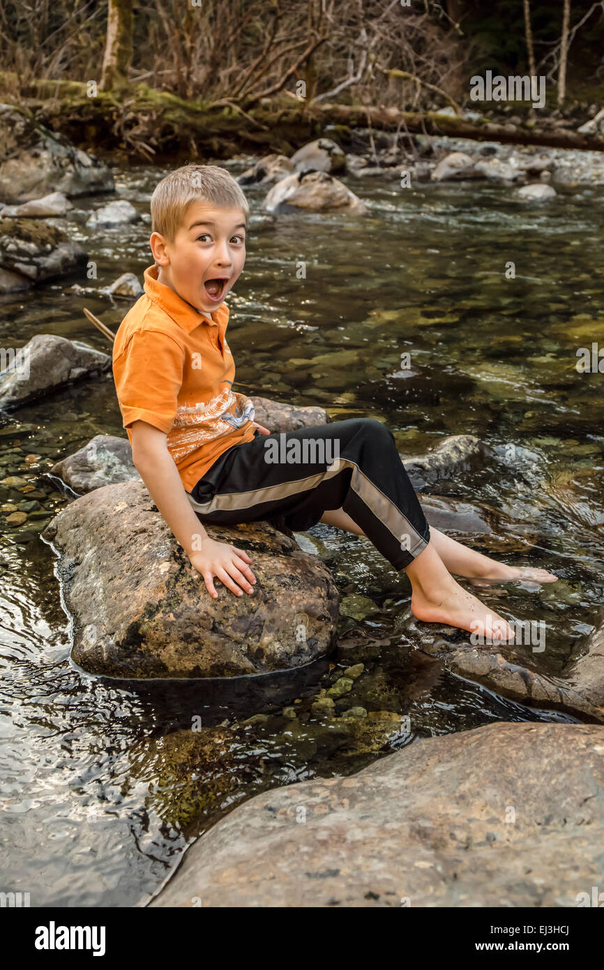 Sieben Jahre alter Junge overacting, wie kalt das Wasser ist während eintauchen seinen Fuß in den Snoqualmie River in North Bend, Washington Stockfoto