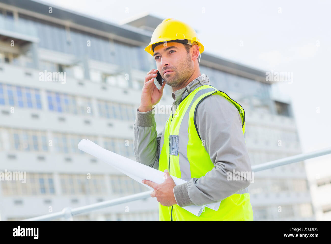 Architekt mit Blaupausen mit Handy gegen Gebäude Stockfoto