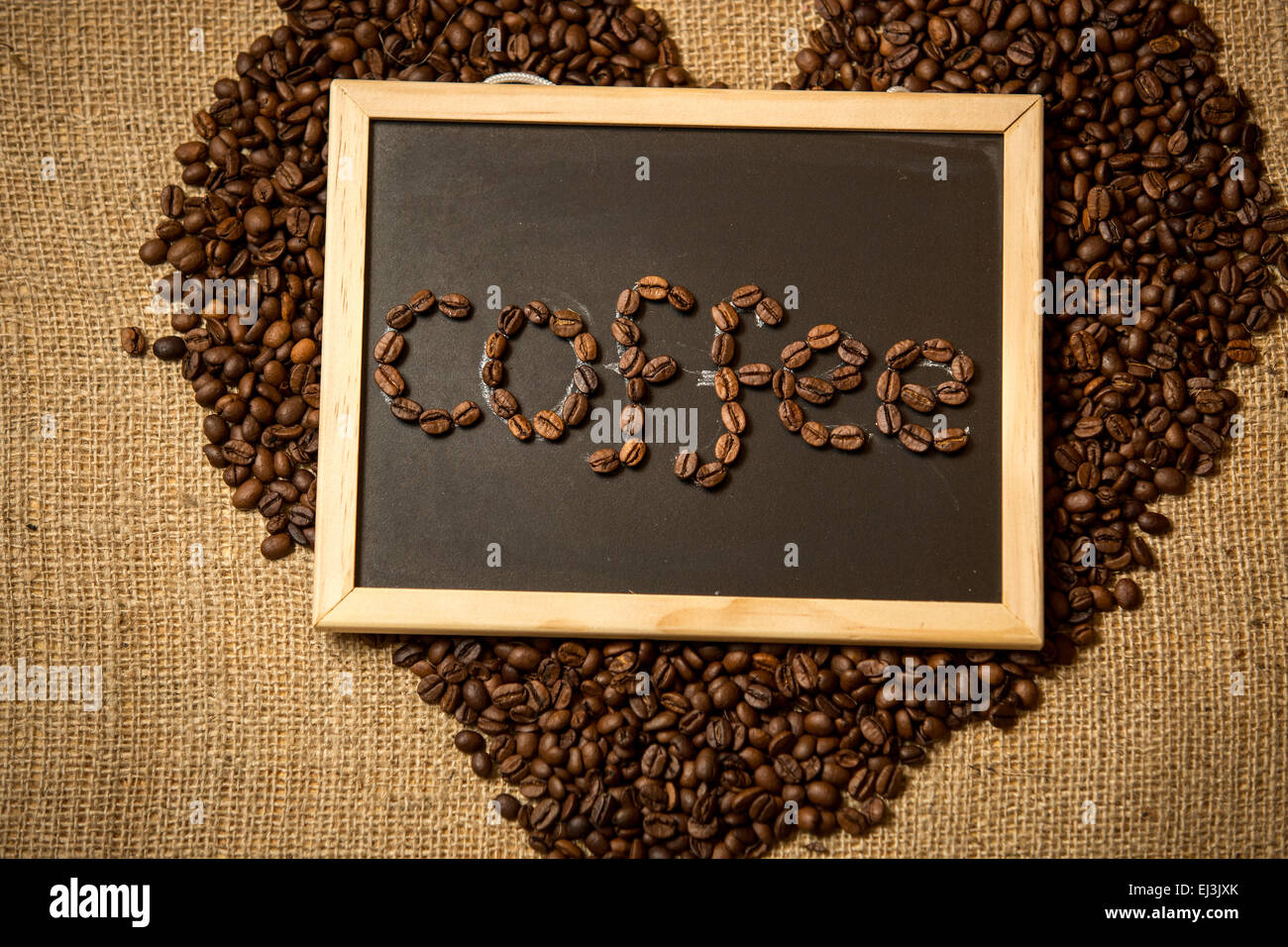 Wort "Kaffee" geschrieben von Kaffeebohnen an schwarze Tafel gegen Leinenstruktur Stockfoto