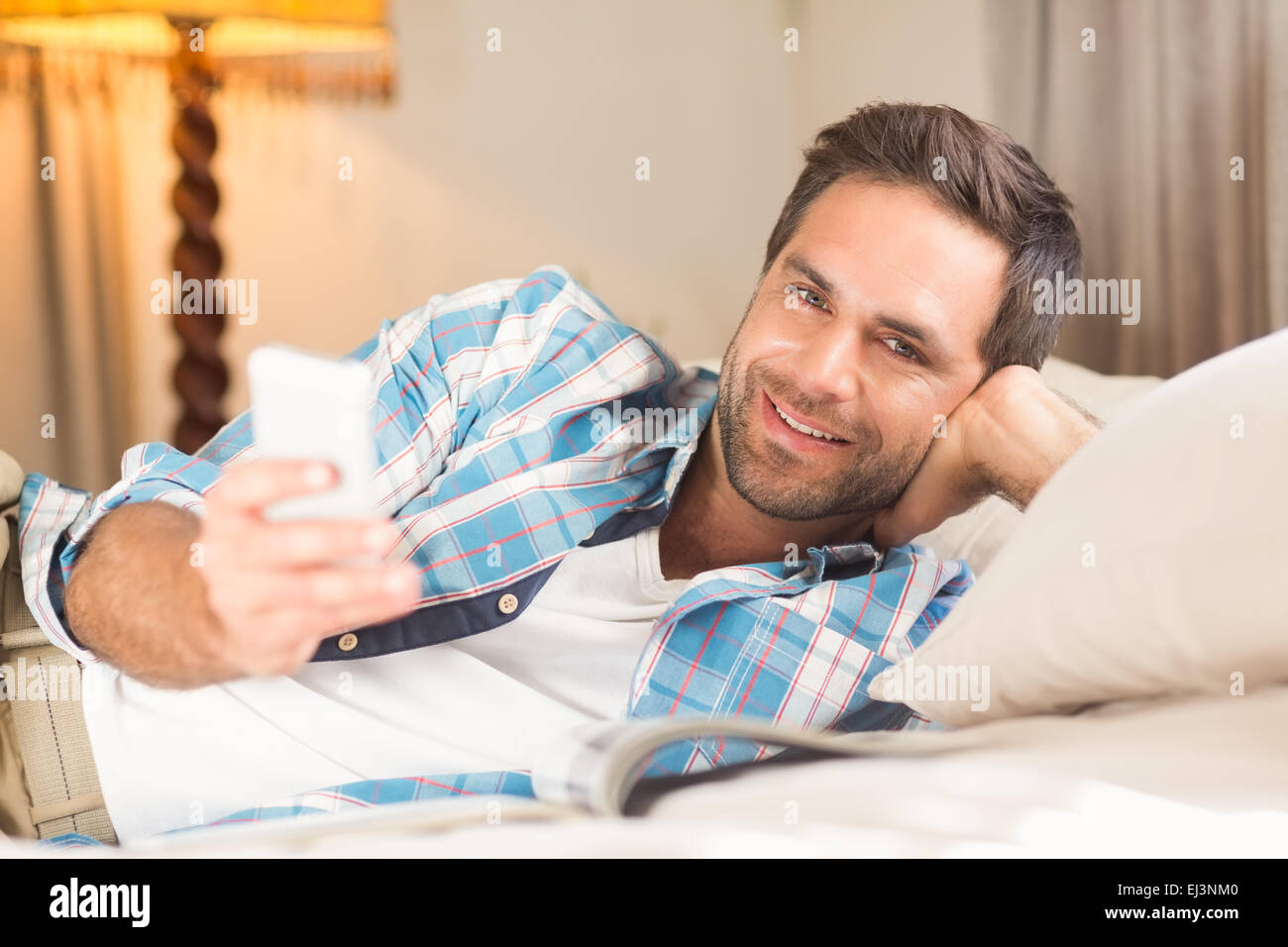 Gut aussehender Mann auf seinem Bett mit Telefon Stockfoto