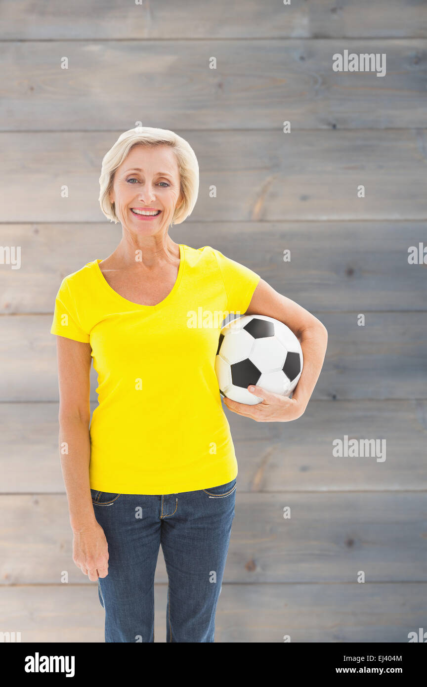 Zusammengesetztes Bild Reife blonde Holding Fußball lächelnd in die Kamera Stockfoto