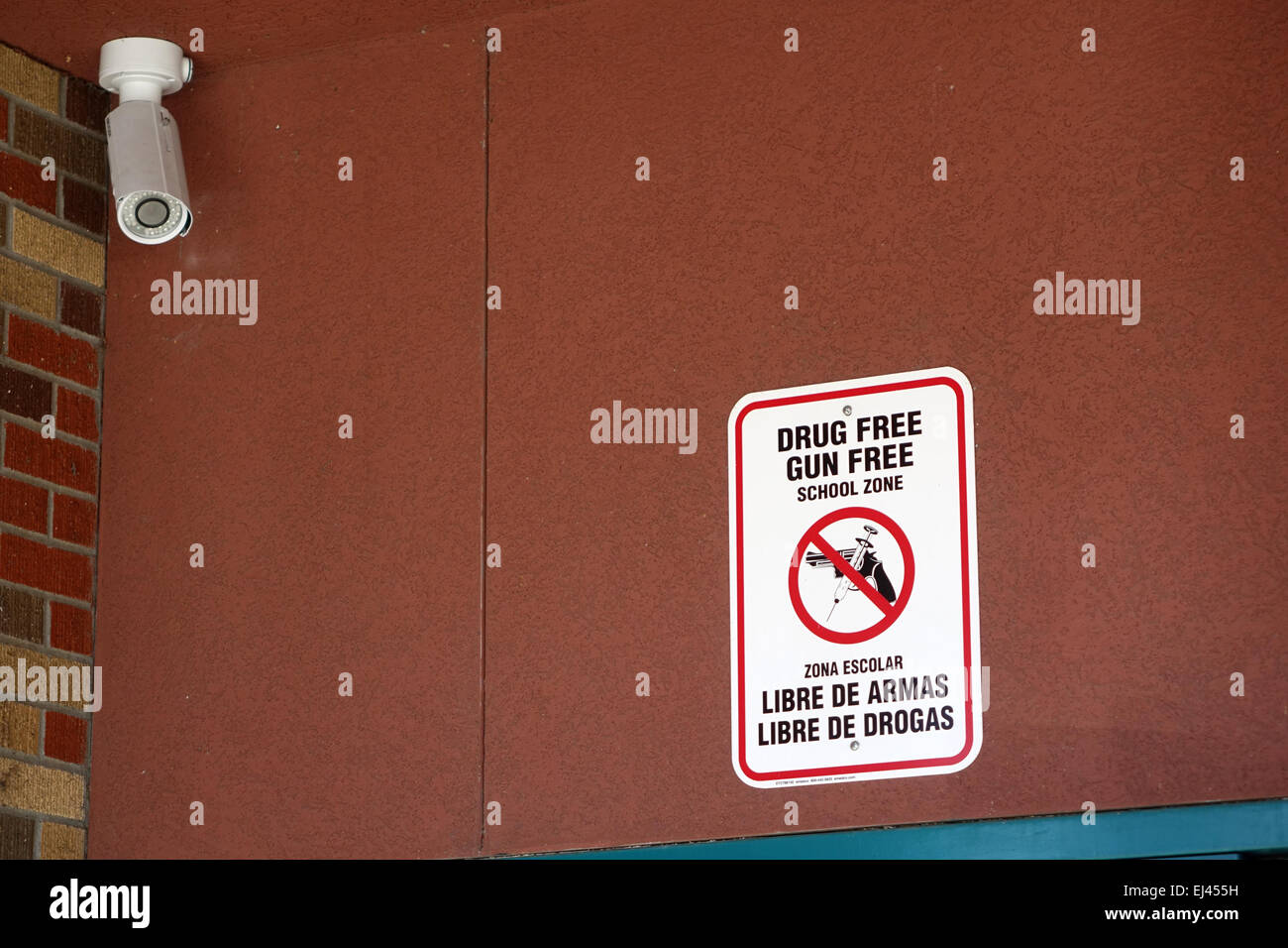 Eine Überwachungskamera Uhren einen Eingang in eine Schule und ein Schild warnt davor, dass die Räumlichkeiten frei von Drogen und Waffe kostenlos in Englisch sind Stockfoto