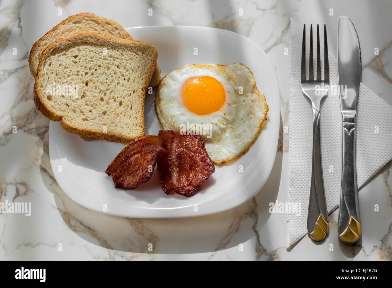Speck mit Eiern auf einem weißen Teller mit Brot Stockfoto