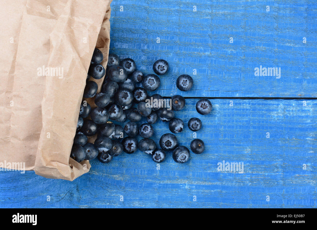 Frisch gepflückte Heidelbeeren aus eine braune Papiertüte auf einem rustikalen blau Holztisch. Querformat mit textfreiraum erschossen Stockfoto