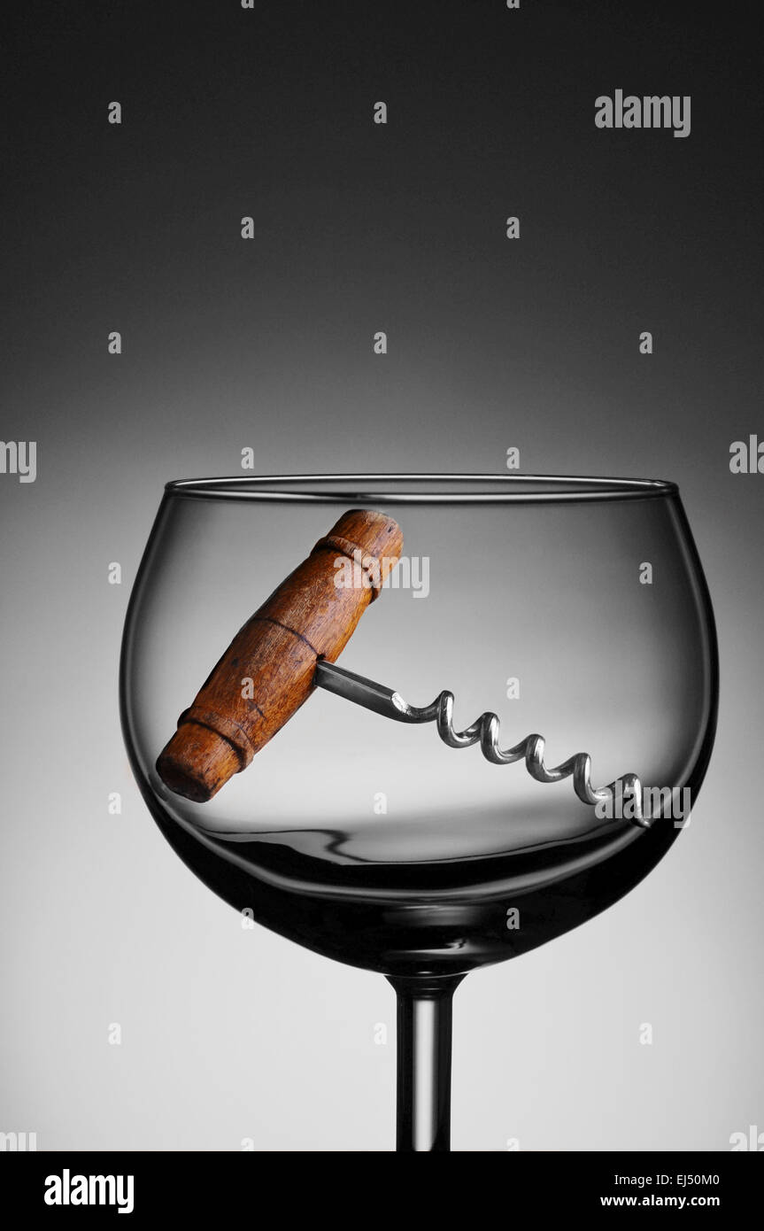 Eine antike Korkenzieher in ein Glas Wein gegen ein Licht, dunkelgrauen Hintergrund. Stockfoto