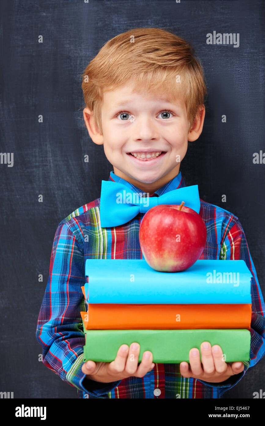 Lächelnde Encoureged Ingwer-junge hält einen Stapel Bücher Stockfoto