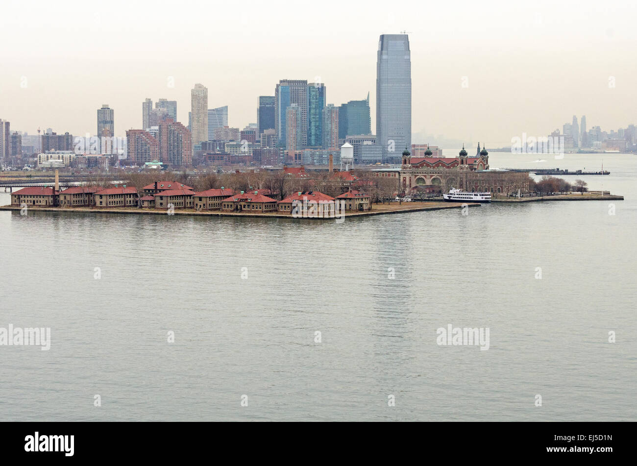Von Liberty Island im Süden betrachtet sind die Isolierstationen von Ellis Island Immigration Museum von den Wolkenkratzern von Jersey City in den Schatten gestellt. Stockfoto
