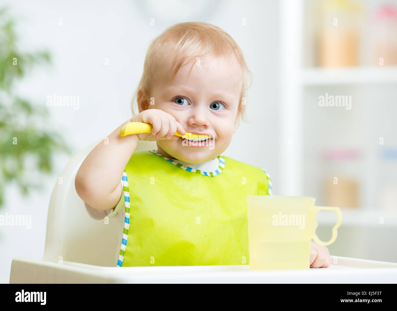 Baby Kind sitzt im Stuhl mit einem Löffel Stockfoto