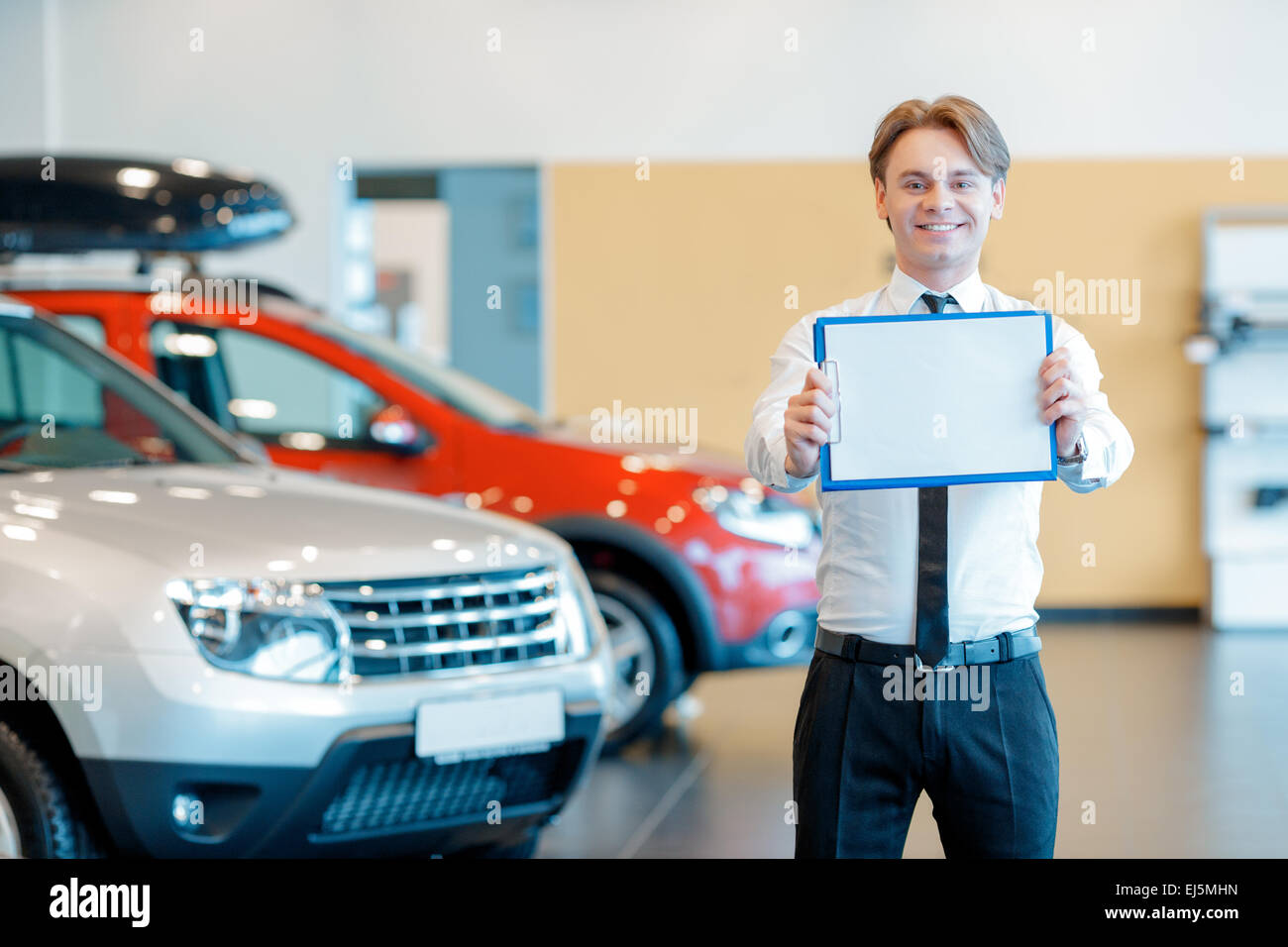 Junge lächelnden Verkäufer mit Zwischenablage im Autohaus Stockfoto