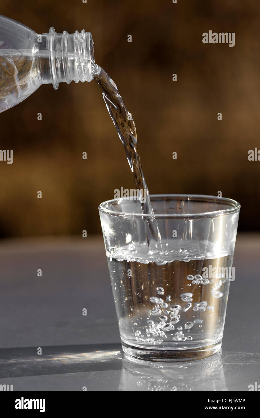 Gießt Wasser aus der Flasche ins Glas auf Natur Hintergrund Stockfoto
