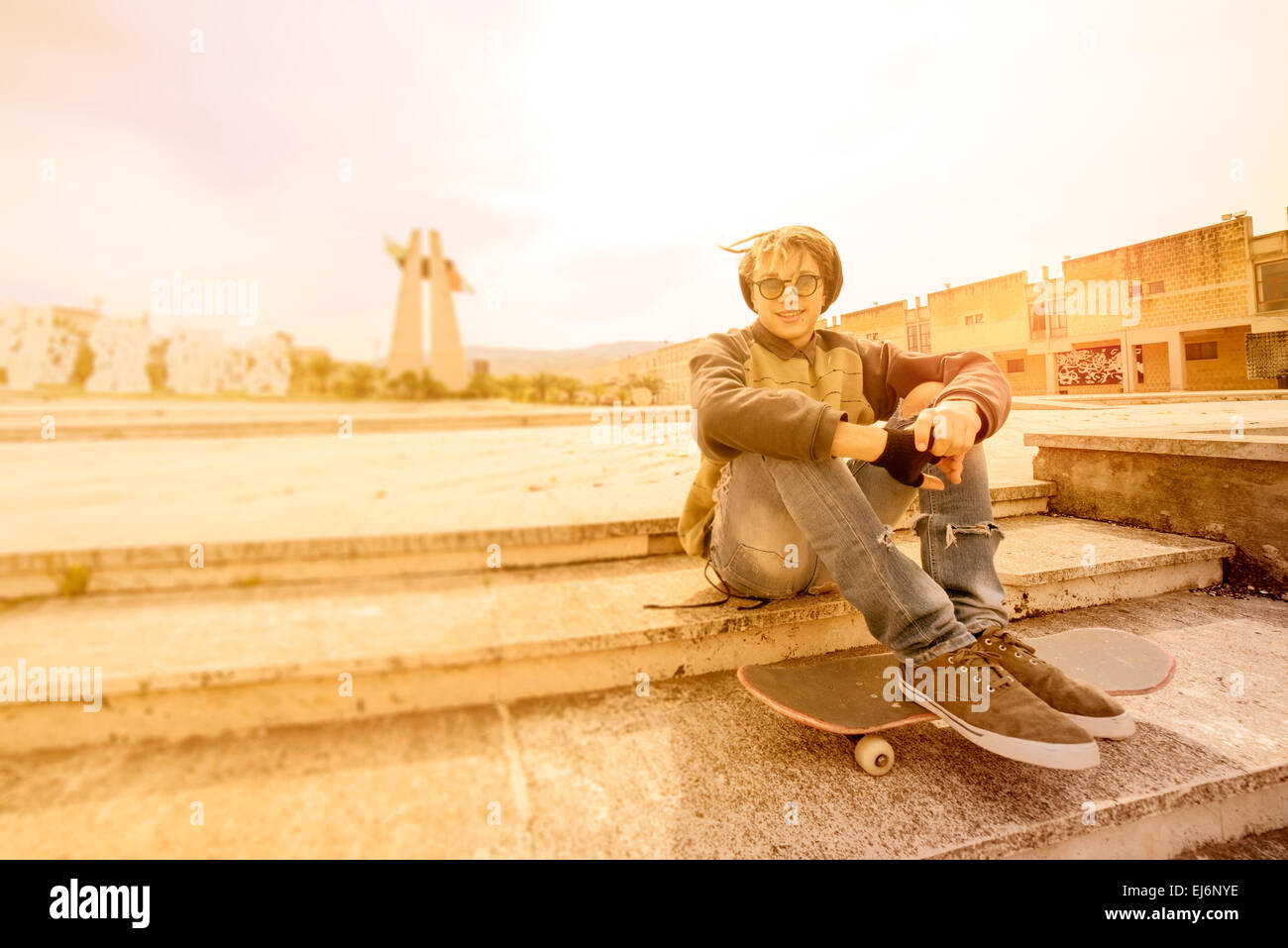 junger Rasta Mann im Freien sitzen auf seinen Skate mit einem warmen Filter angewendet Stockfoto