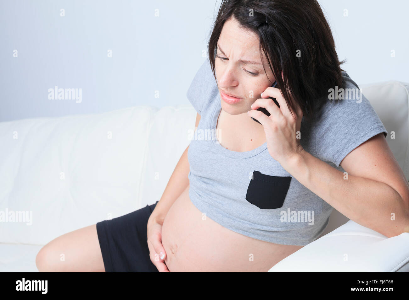 Schwangere Frau mit einem Telefon auf dem Sofa sitzen Stockfoto