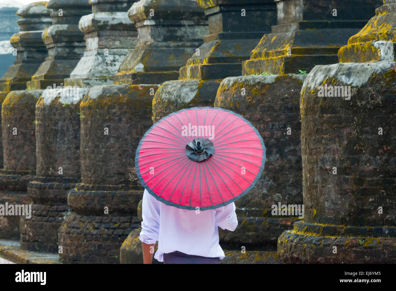 Mann mit roten Regenschirm zu Fuß durch Pagoden der Shitthaung Tempel, Mrauk U, Rakhine State in Myanmar Stockfoto