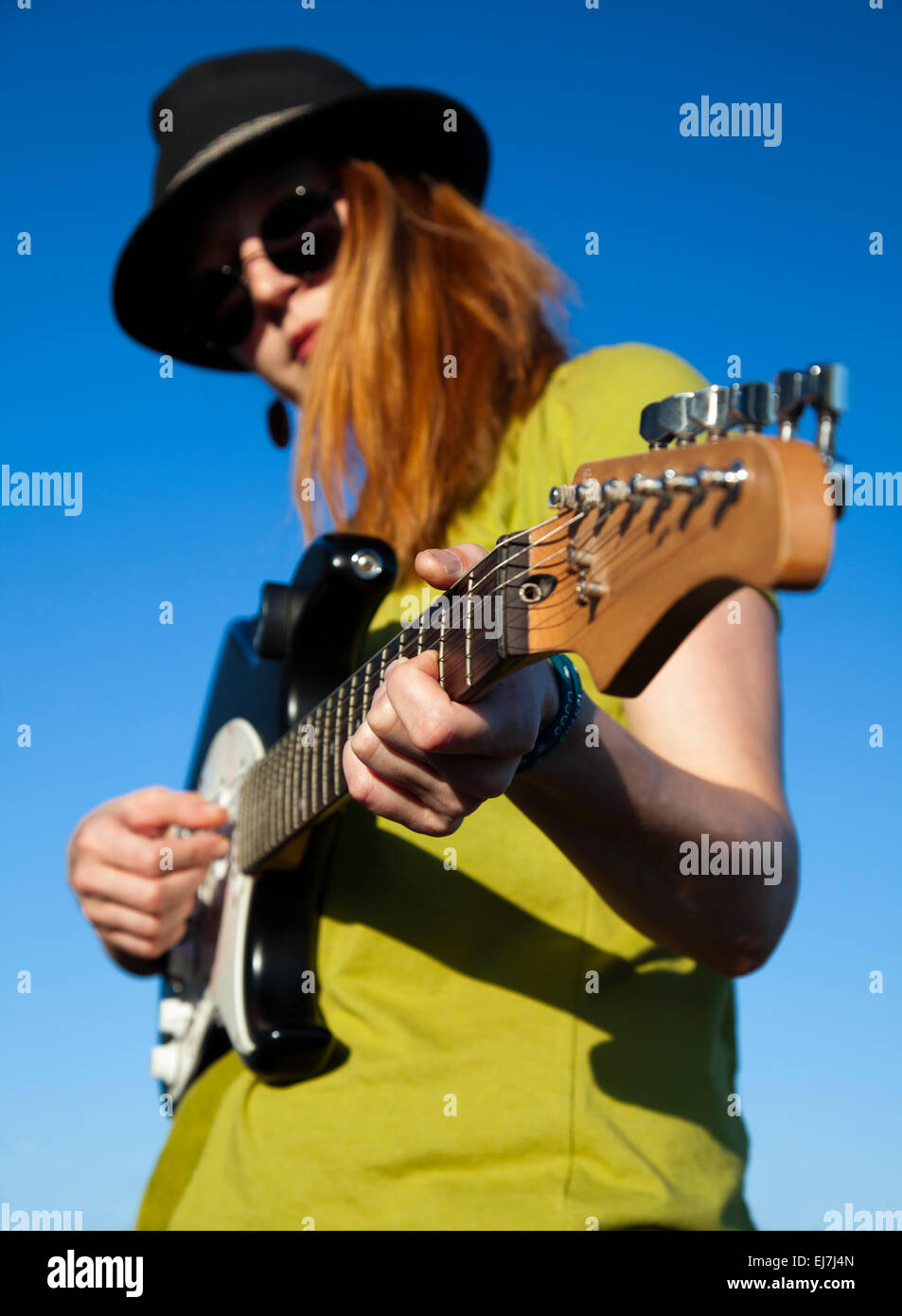 Weibliche Busker mit Gitarre stilvolle Musikerin mit roten Haaren Träger in schwarzen Hut und grünes Hemd spielt auf der Gitarre. Stockfoto