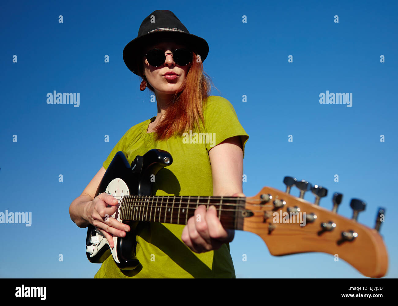Weibliche Busker mit Gitarre stilvolle Musikerin mit roten Haaren Träger in schwarzen Hut und grünes Hemd spielt auf der Gitarre. Stockfoto