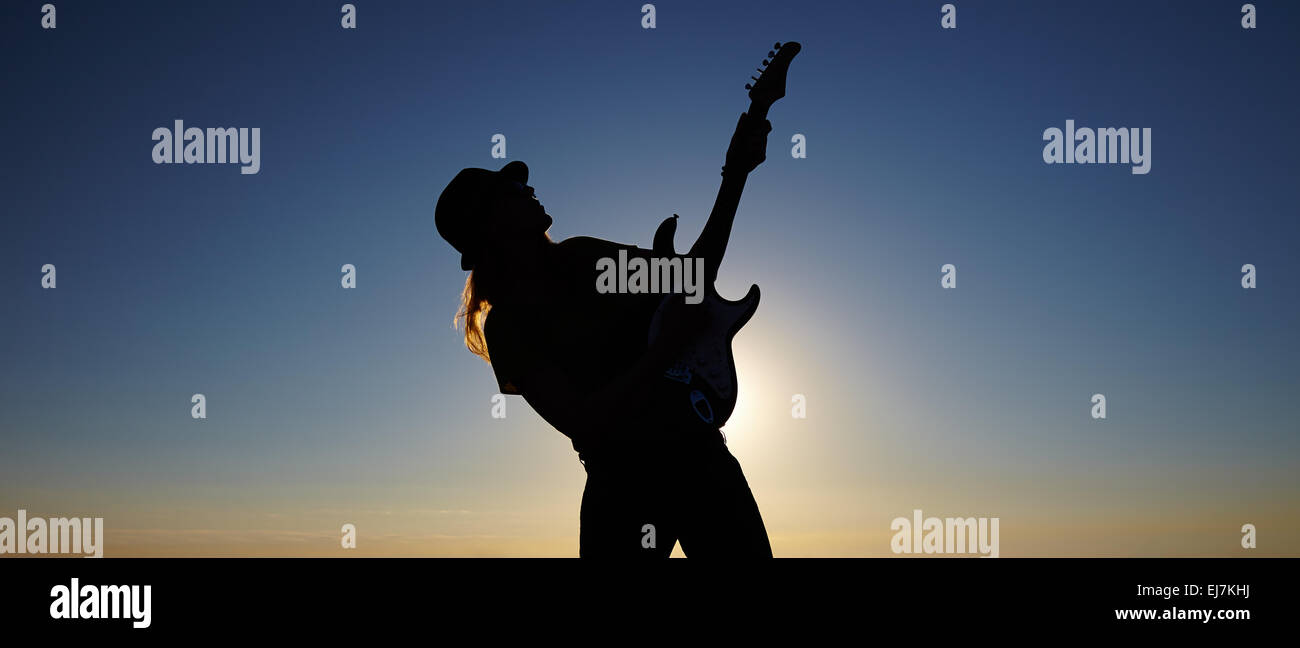 Silhouette des weiblichen Straßenmusiker vor Sonnenaufgang. Biegen Körper der weiblichen Musiker halten die Gitarre auf dem aufgehenden Sonne-Hintergrund Stockfoto