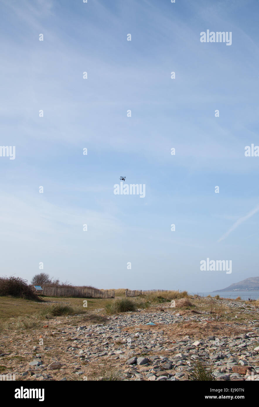 Eine Fernbedienung, die fliegenden Kameradrohne schwebt über dem Strand vor einem blauen Himmel in Conwy Hafen / Strand, Nordwales Stockfoto