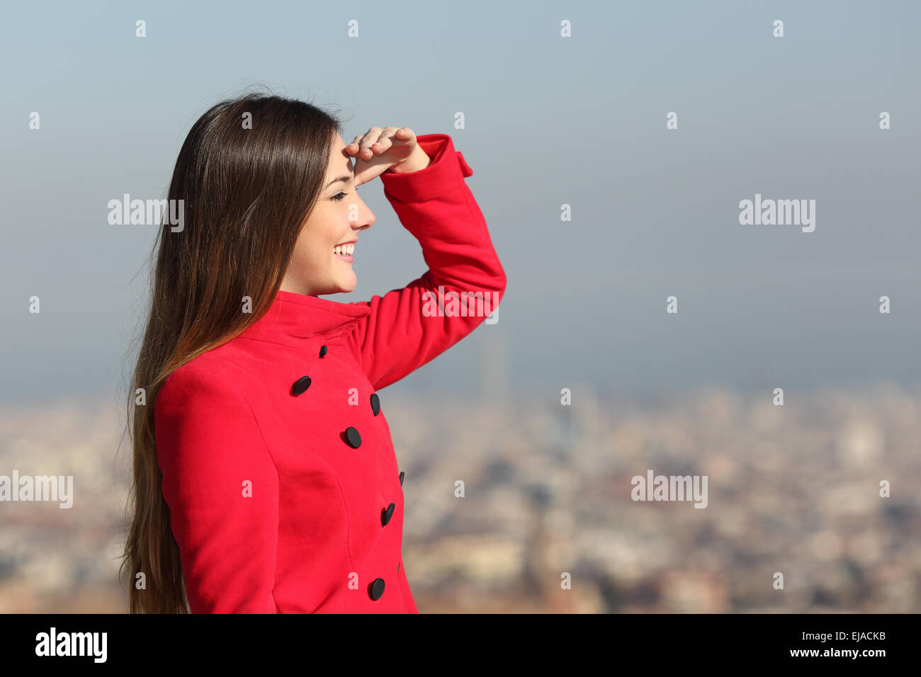 Frau freut sich im Winter mit einem roten Mantel mit Stadt im Hintergrund Stockfoto