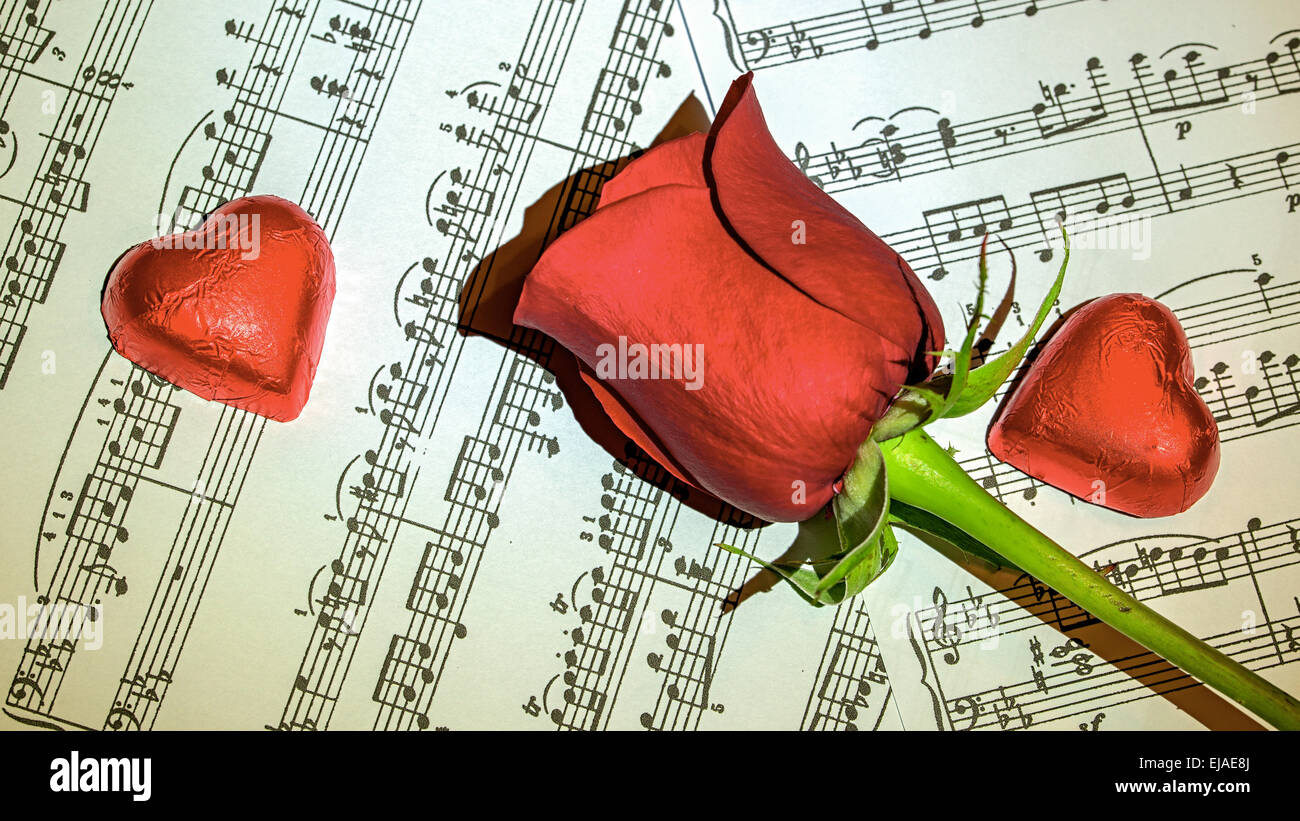 Rote Rose auf Partituren mit Schokoladenherzen rund um Stockfoto