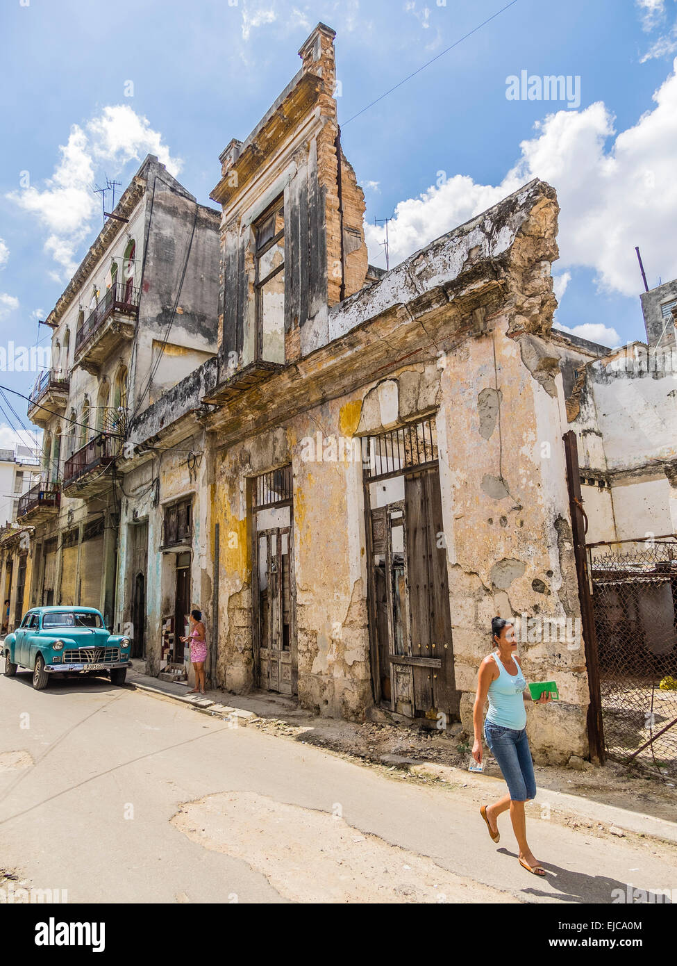 Hispanic Frau geht vorbei an der 1950er Jahre Oldtimer und einer verlassenen, bröckelt, aufbauend auf einer Straße in Havanna, Kuba. Stockfoto