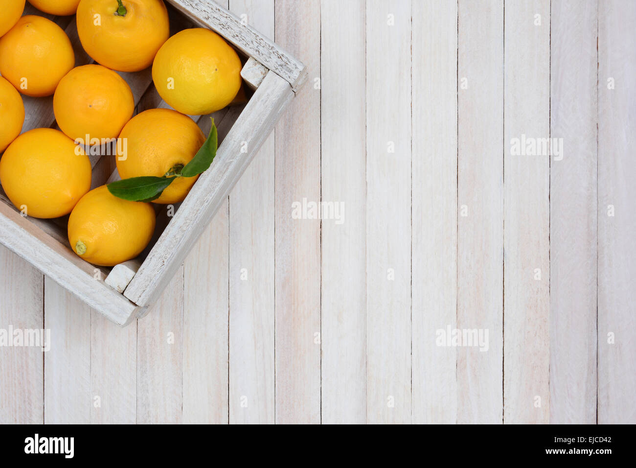 Eine Kiste mit frisch gepflückten Zitronen auf einen rustikalen weißer Holztisch in der oberen linken Ecke des Rahmens. Querformat Stockfoto