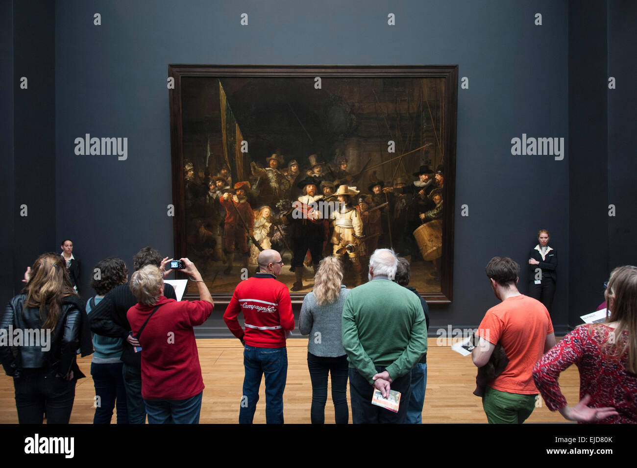 Besucher stehen vor dem Gemälde "Nachtwache" von Rembrandt van Rijn bewacht von zwei Museumswärter im Rijksmuseum, Amsterdam, Niederlande Stockfoto