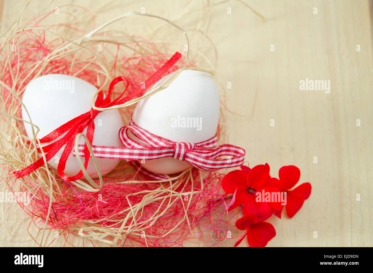 Zwei weißen Eiern mit Bändern befestigt, liegend in einem Nest mit zwei roten Blüten Stockfoto