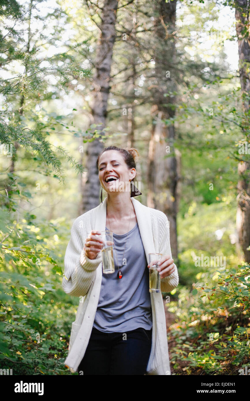 Eine Frau steht auf einer Lichtung im Wald hält zwei große Gläser Champagner. Stockfoto