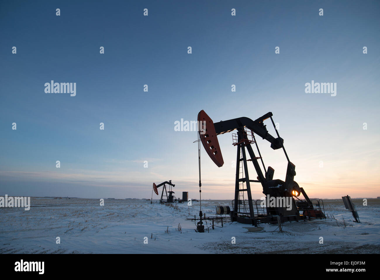 Ein Öl-Bohr-Rig und Bohrschwengels auf einer flachen Ebene in den kanadischen Ölfeldern bei Sonnenuntergang. Stockfoto