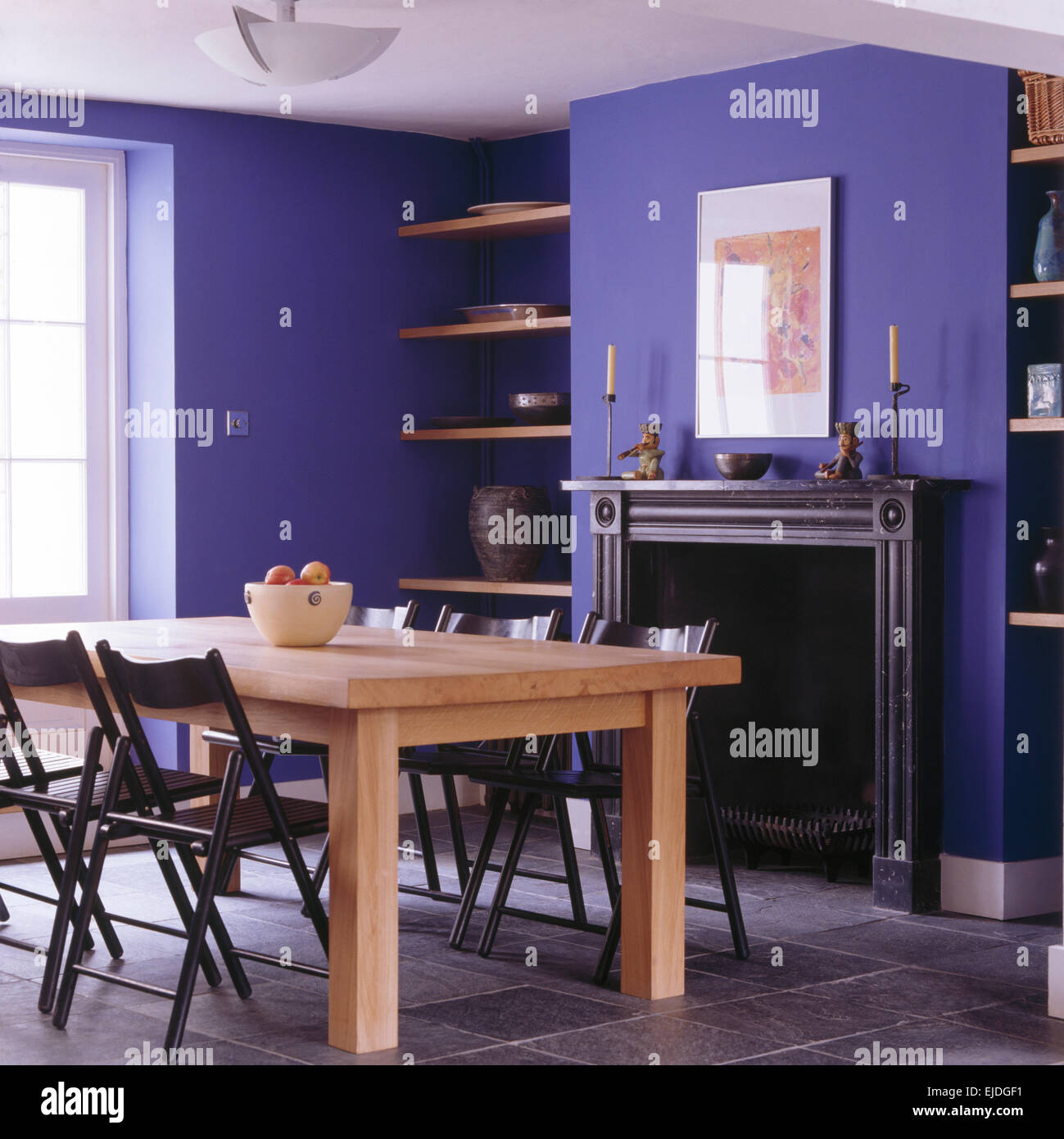 Schwarz, Klappstühle bei einfachen Holztisch im hellen blauen Speisesaal mit Schiefer Kamin und Fliesenboden Stockfoto