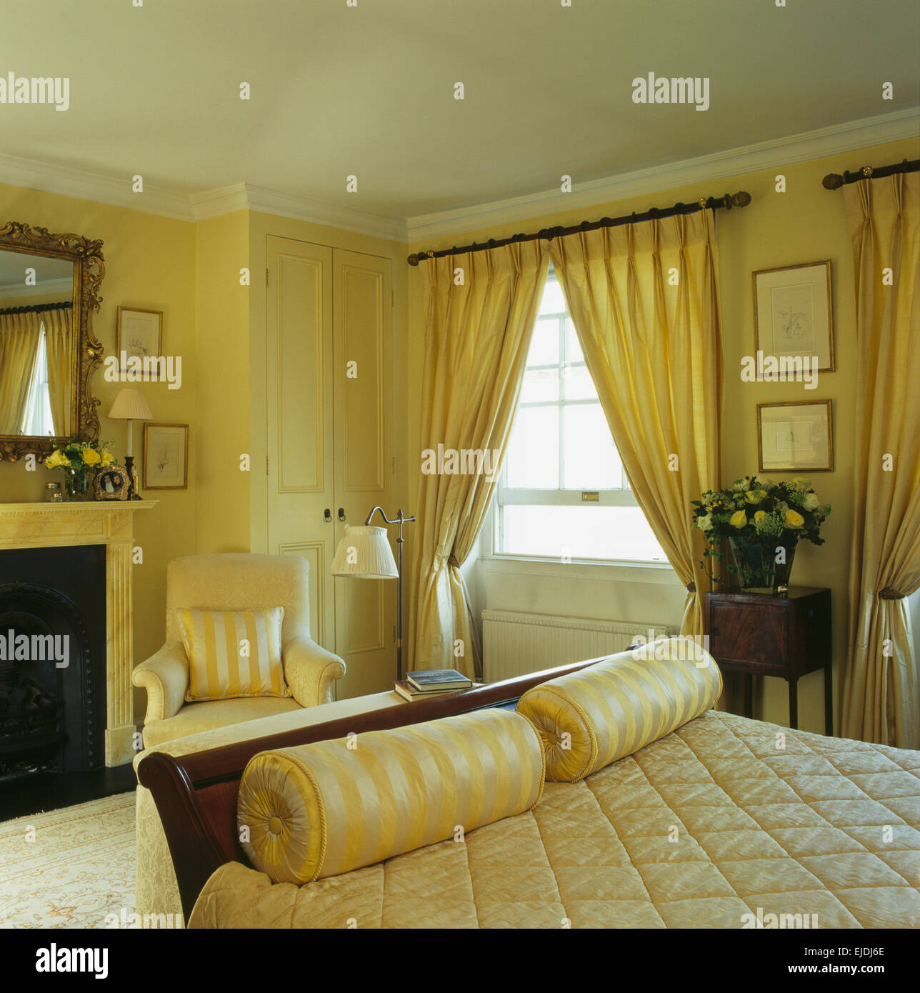 Gelbe Seide Nackenrolle Kissen am Fuße des Bettes im Schlafzimmer Gelb Stadthaus mit gelben Vorhänge am Fenster Stockfoto
