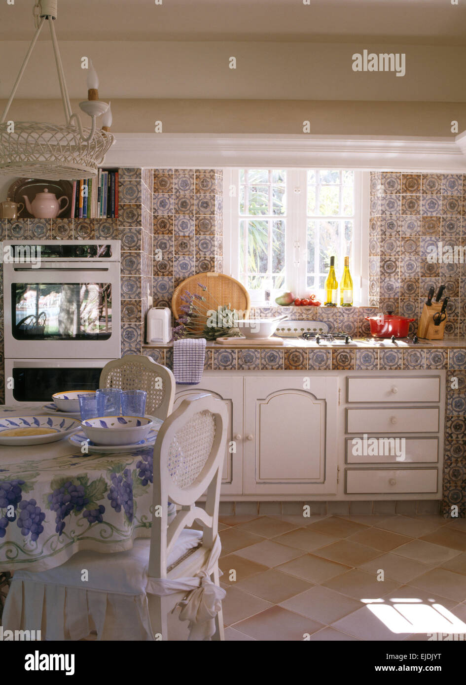 Gemusterte Fliesen und Arbeitsplatte in französische Landküche mit weiß lackierten Stühle am Esstisch Stockfoto