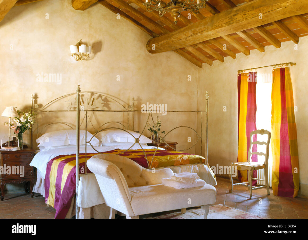 Kleine Chaiselongue am Fuße des reich verzierten schmiedeeisernen Bett mit bunt gestreiften Seide werfen im toskanischen Schlafzimmer Stockfoto