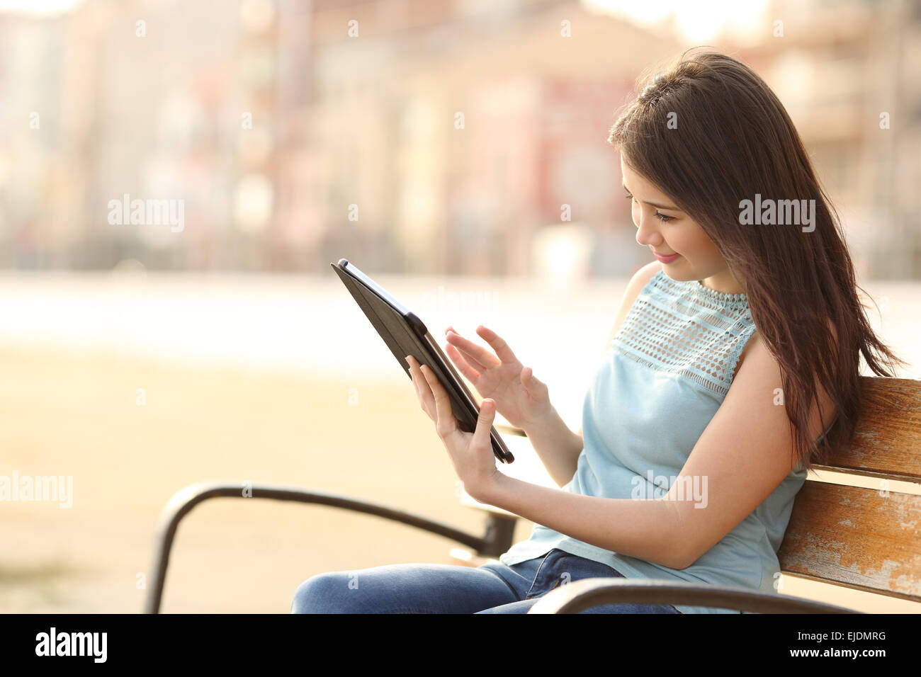 Mädchen lesen und Surfen, ein Ebook oder ein Tablet sitzen in einer Bank in einem park Stockfoto