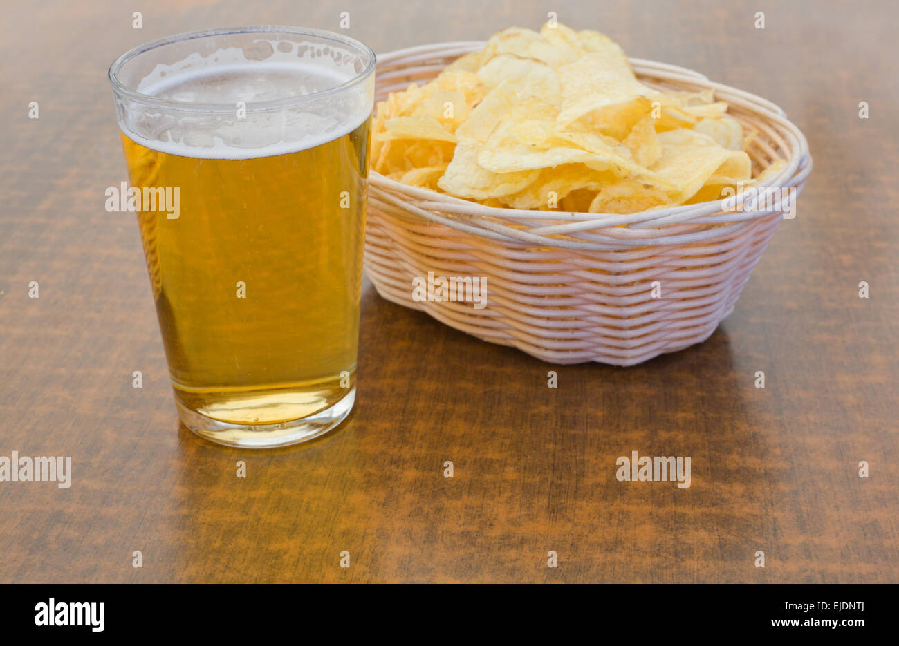 Glas Bier mit Chips auf Weidenkorb über Holztisch Stockfoto