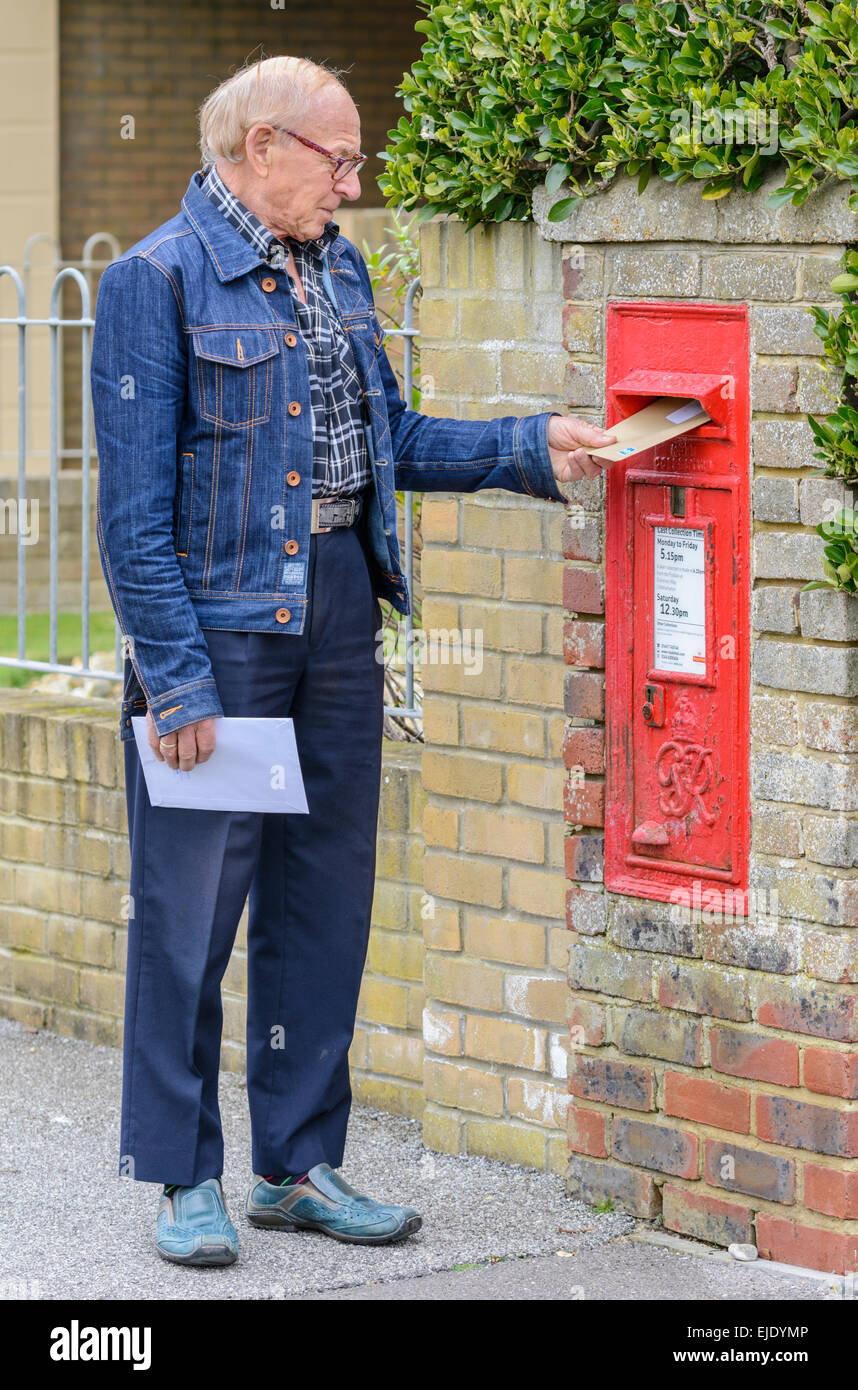 Älterer Mann Entsendung einen Brief in einer Royal Mail Wand montiert Briefkasten in England, UK. Stockfoto