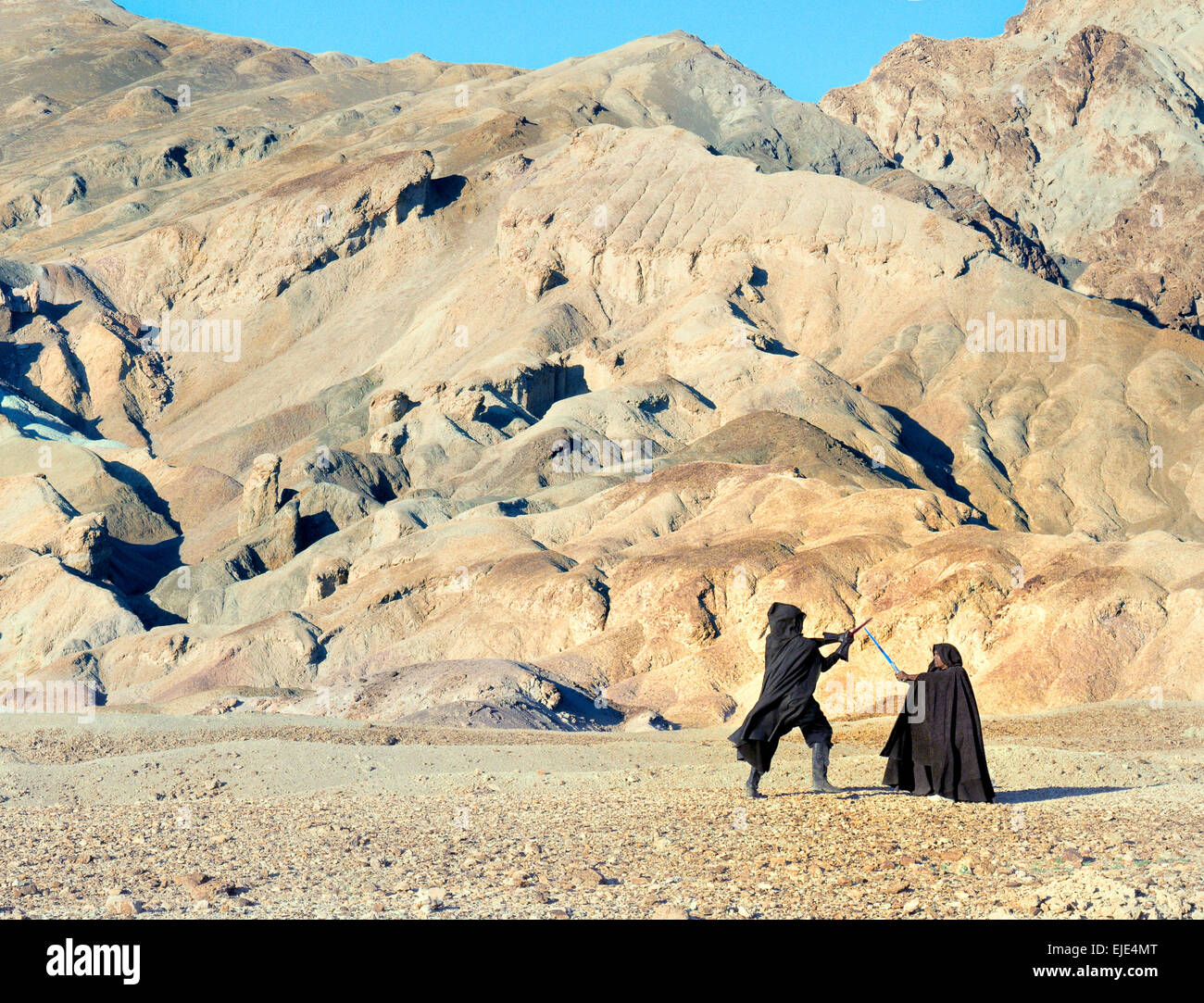 Im Death Valley duellieren sich zwei Reenactoren in dunklen Mänteln mit Lichtschwertern vor einer rauen Wüstenkulisse, um eine klassische Szene aus „Star Wars“ nachzubilden. Stockfoto