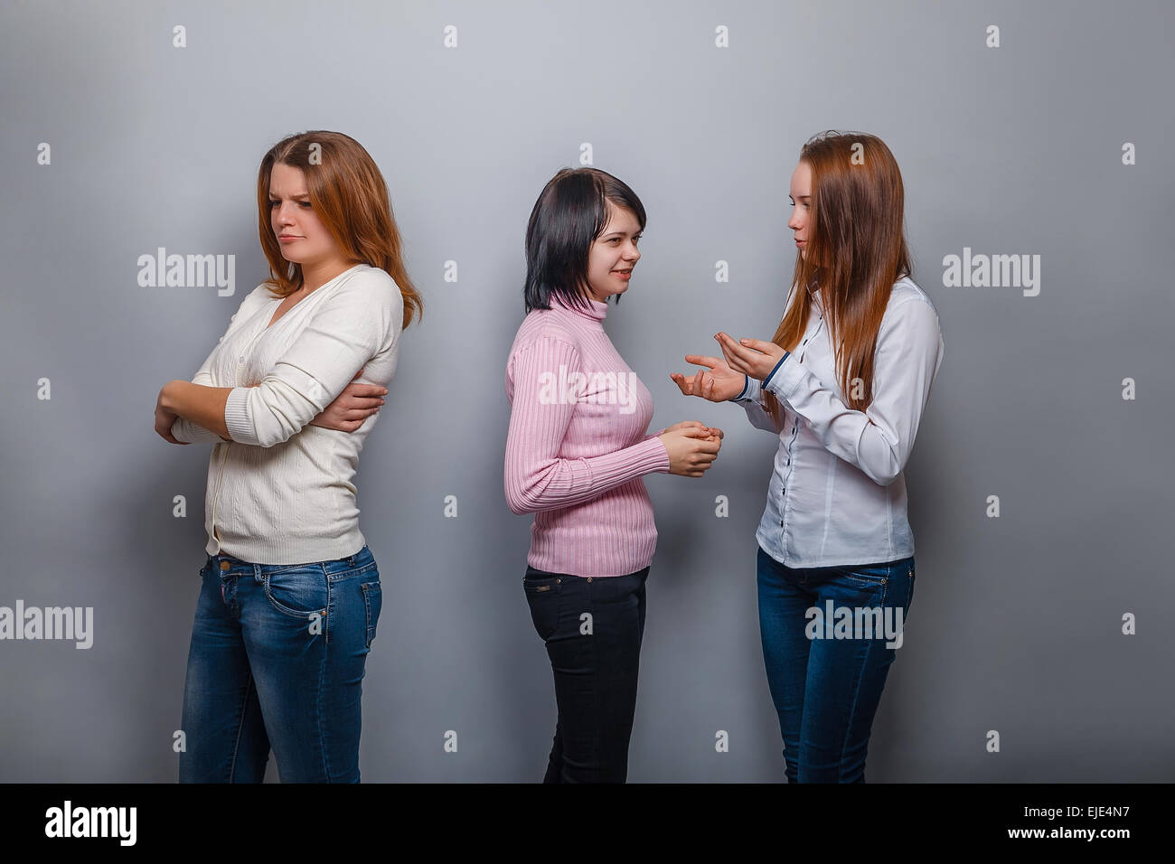 Zwei Mädchen reden blonde europäischen aussehen und ignorieren das dritte Mädchen auf einem grauen Hintergrund, Groll, Traurigkeit Konflikt Freund Stockfoto