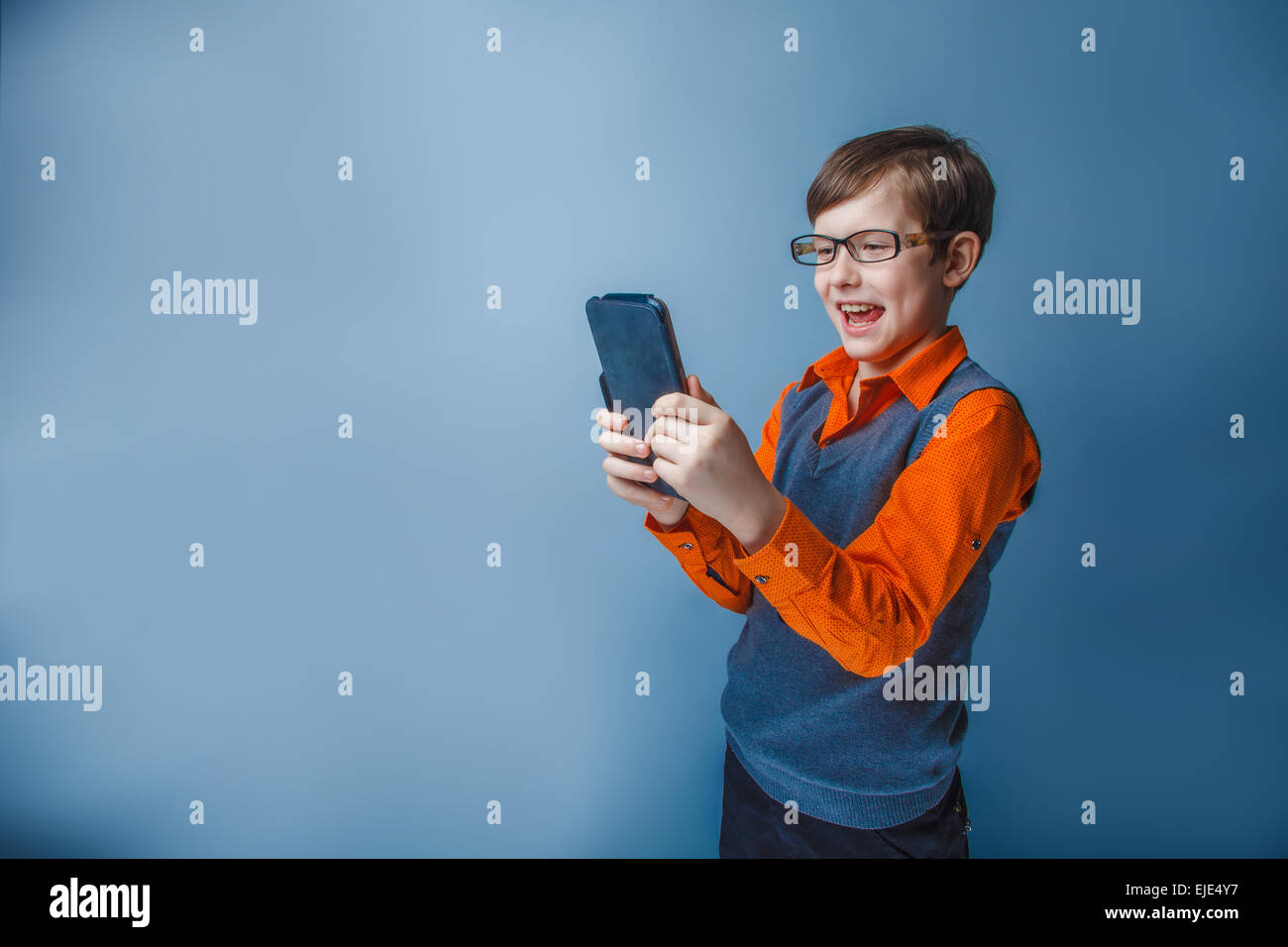 Europäisch anmutende junge von zehn Jahren in Gläser halten Tablet in der hand, spielt, Vergnügen auf blauem Hintergrund Stockfoto