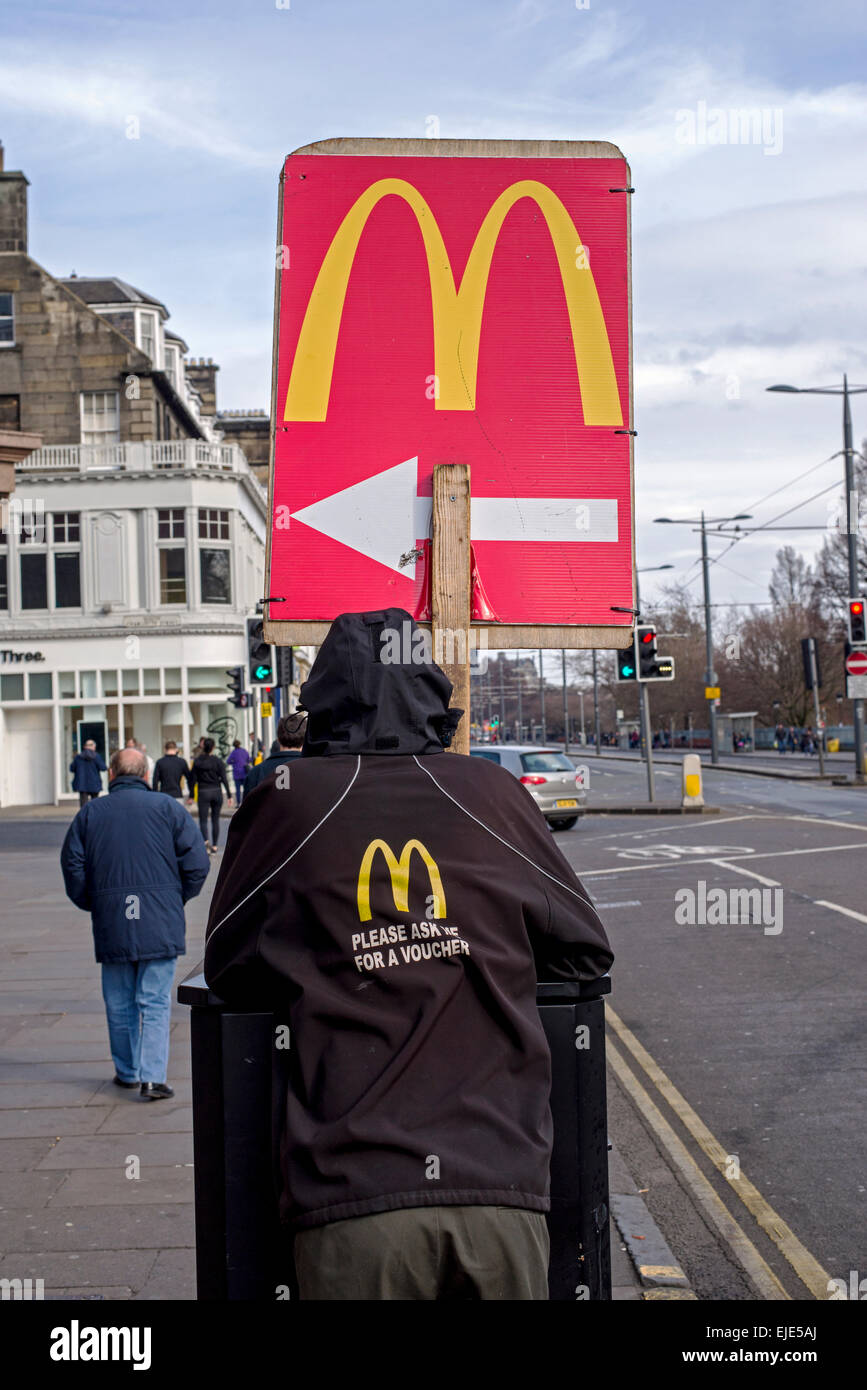 Ein junger Mann hält ein Wegweiser in eine Filiale von McDonalds auf der Princes Street, Edinburgh, Schottland, UK. Stockfoto